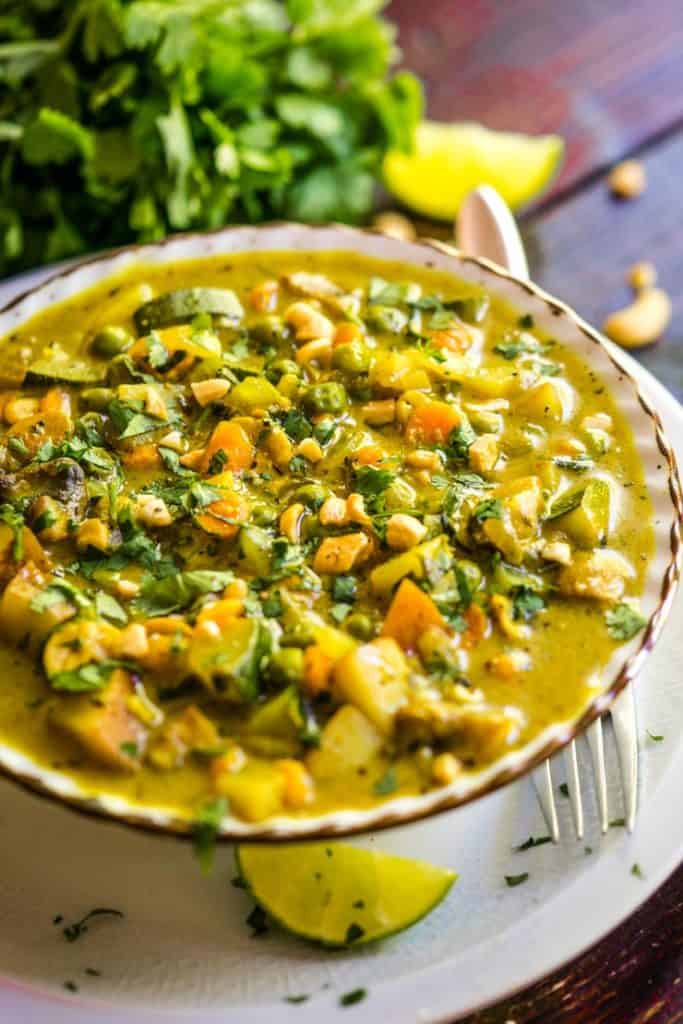 A bowl of vegetable curry sprinkled with cashews and cilantro. 