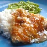 Baked chicken with orange sauce and white rice and green beans on a blue plate