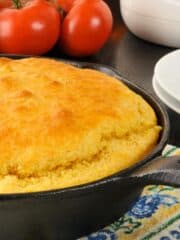 The best cornbread in a cast iron skillet with tomatoes in the background