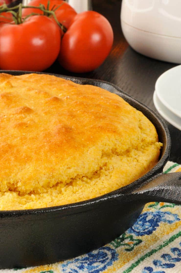 The best cornbread in a cast iron skillet with tomatoes in the background