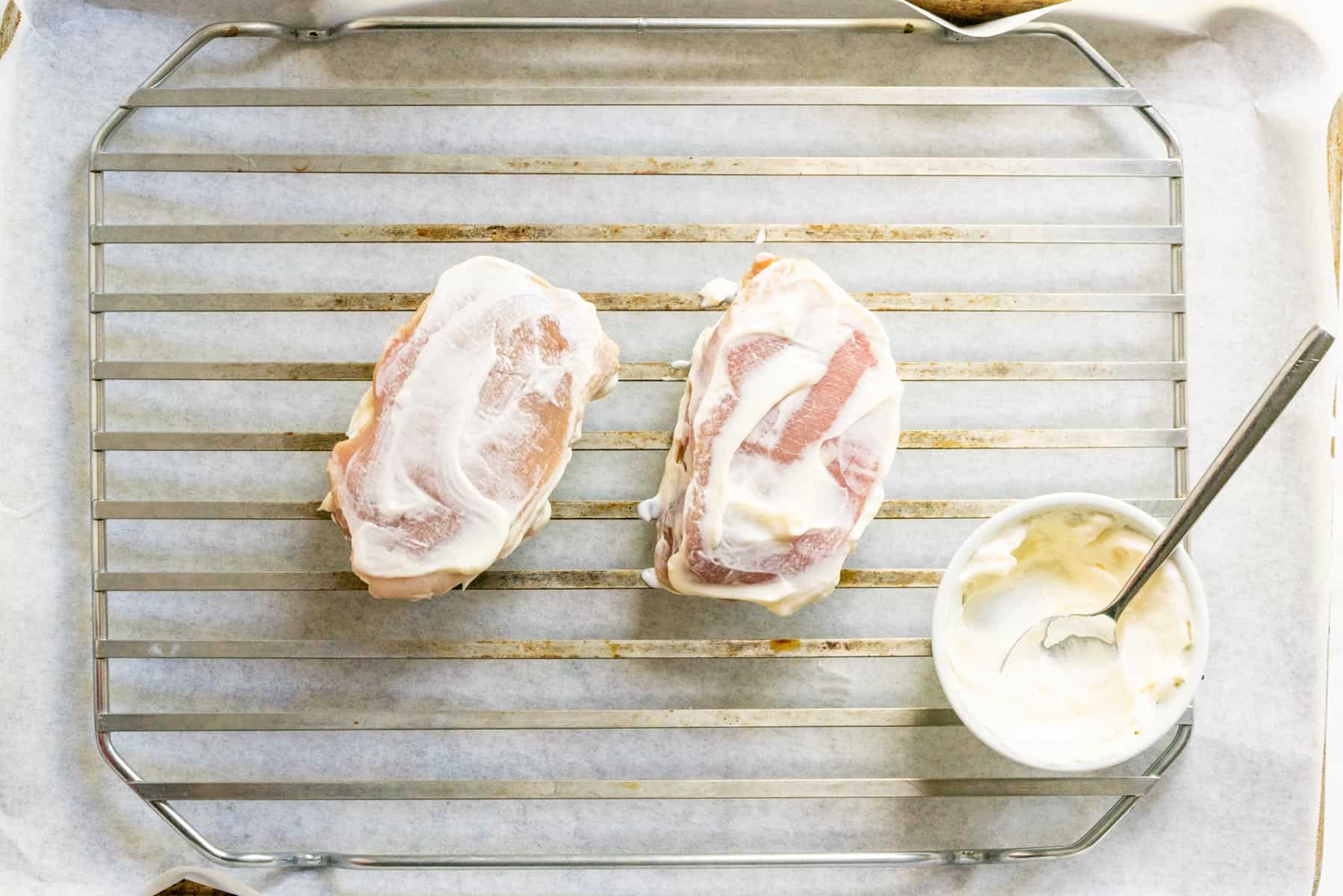 2 pork chops with mayonnaise on them on a wire rack