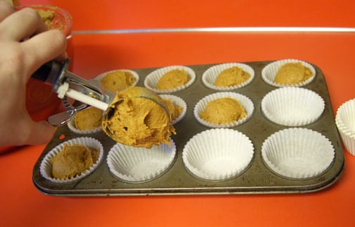 muffins being scooped into a muffin tin with white liners