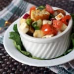 Panzanella Salad in white bowl on top of a lettuce leaf in another white bowl on a placemat with a fork