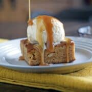 Caramel blondie brownie with a scoop of ice cream and caramel drizzled on top on a white plate