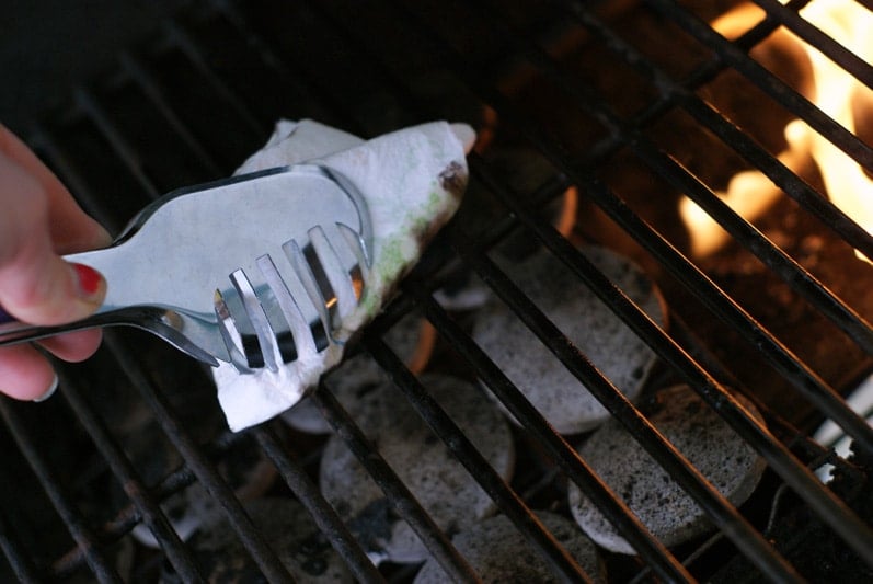 tongs holding a paper towed dipped in oil to oil grill grates