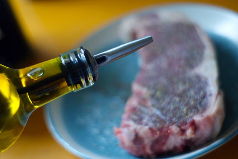 close up of olive oil bottle with steak in background