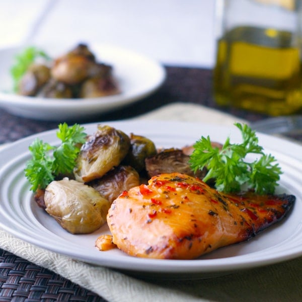 baked chili salmon on a white plate with parsley and brussels sprouts