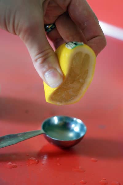 lemon being squeezed into a measuring spoon