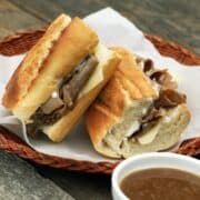 French dip sandwiches on a wicker plate with a bowl of au jus