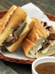 French dip sandwiches on a wicker plate with a bowl of au jus