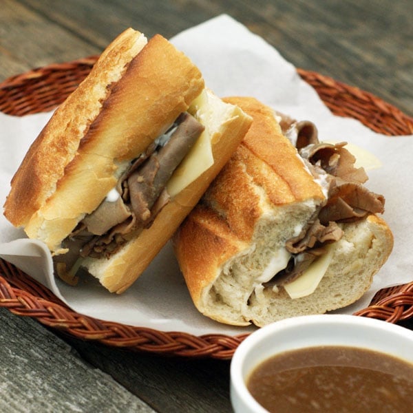 French Dip Sandwiches on a wicker plate with a bowl of au jus
