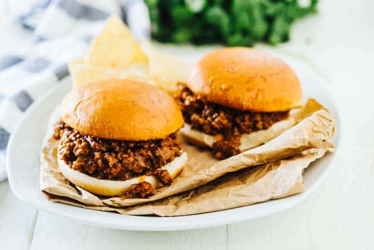 2 sloppy joes on a white plate with potato chips