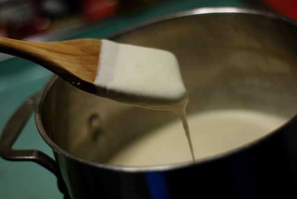 Bechamel sauce on a wooden spoon over a metal pot