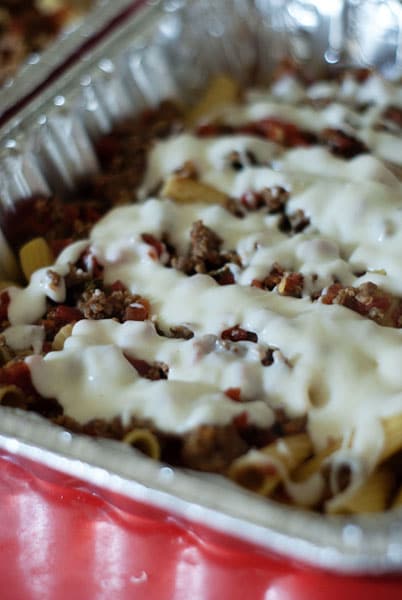 bechamel sauce drizzled over meat sauce and pasta in foil pans