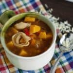 tortellini soup with squash in a green and white mug on a rainbow napkin