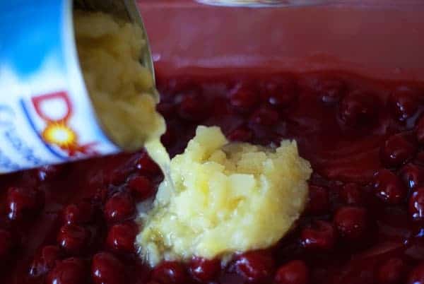 canned pineapple being poured on top of the cherries in a glass dish