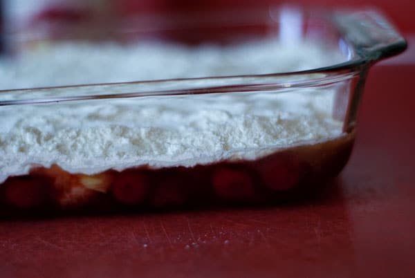 yellow cake mix spread out on top of the fruit in a baking dish