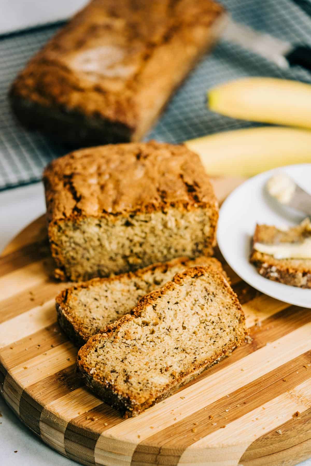 Loaf of banana bread and 2 slices on a striped wood cutting board