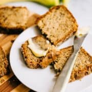Sliced banana walnut bread on a white plate with butter