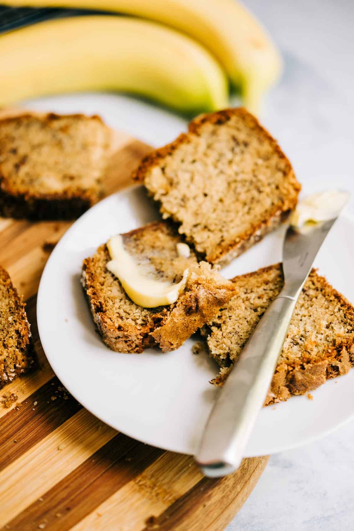 Sliced banana bread on a white plate with butter on a striped cutting board