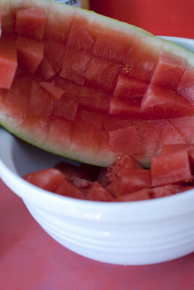 Pouring watermelon cubes into a white bowl.