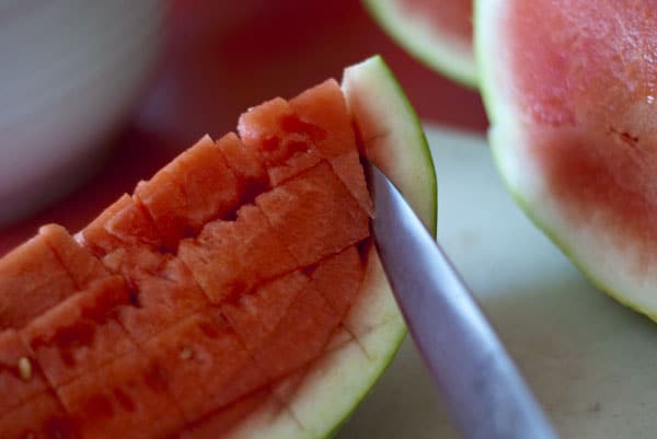 Using a knife to cut into a watermelon and making diced watermelon.