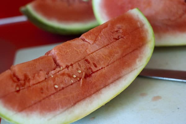Lines cut on a slice of watermelon on a white cutting board.