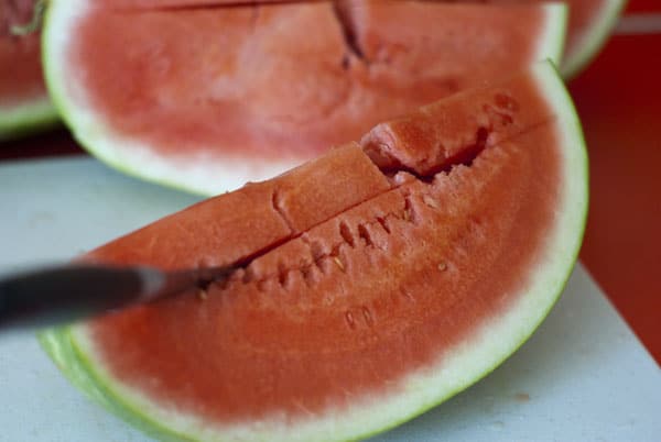 Cutting into a slice of watermelon on a white cutting board.