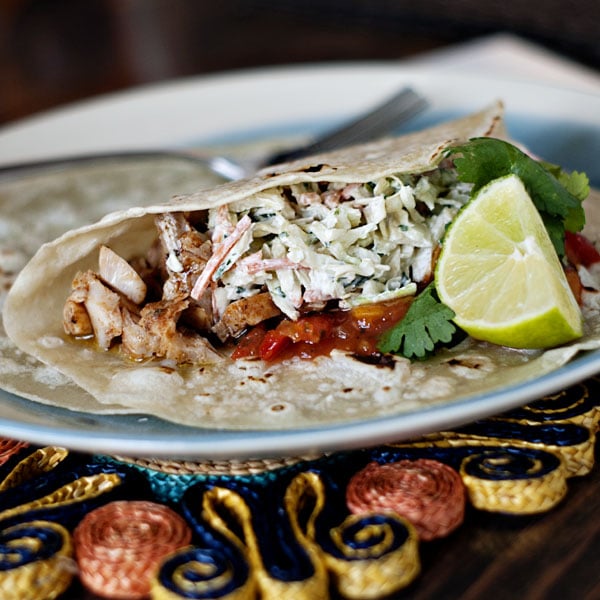 Broiled Fish Tacos in tortillas on a white and blue plate with limes