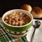 Smoky Ham, Bean, Sweet Potato Soup in a green and white bowl and napkin with rolls