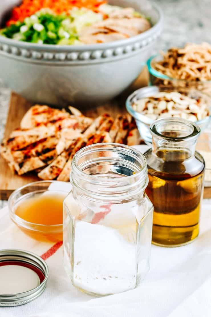 Glass bottles of sugar and oil and a glass bowl of vinegar with an Asian chicken salad in the background.