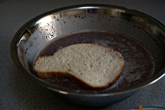 Dipping bread into french toast mix in a mixing bowl.