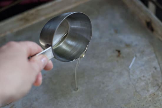Pouring vegetable oil on a baking sheet with a measuring cup.