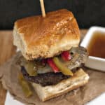 Easy French Dip Burger with bell peppers and sweet onions on a wooden table.