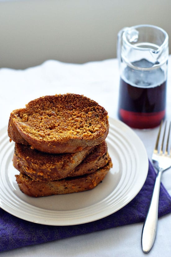 Really Crunchy French Toast stacked on top of a white plate next to a glass of syrup and a silver fork.