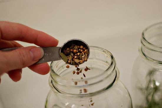 Adding pickling spice into a glass mason jar with a metal measuring spoon.