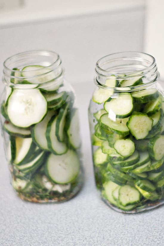 Homemade pickles in two glass mason jars on a table.