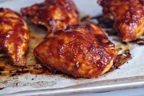 Baked chicken breast on a baking sheet covered in bbq sauce