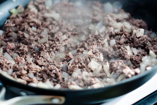 Ground beef and onions cooking in a large skillet.