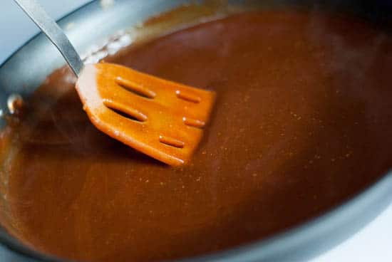 Mixing enchilada sauce in a skillet with a spatula.