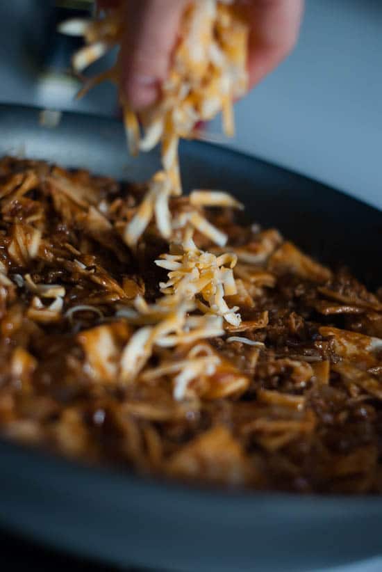 Sprinkling colby jack cheese over homemade Beef Enchilada recipe in a skillet.