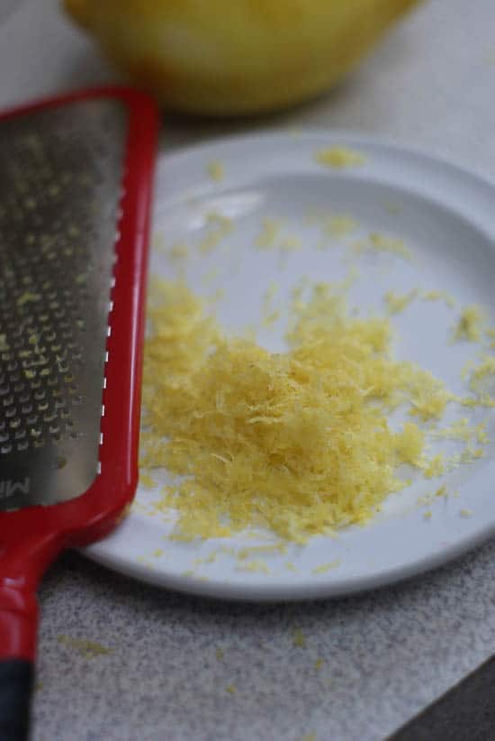 Removing the zest from a lemon onto a small white plate.