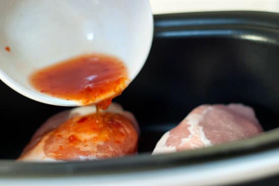 Pouring fish sauce over pork shoulders in a slow cooker.