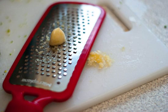 Grating garlic on a white cutting board.
