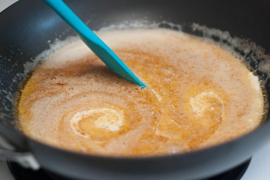 Mixing browned butter and sour cream in a black skillet with a blue spatula.