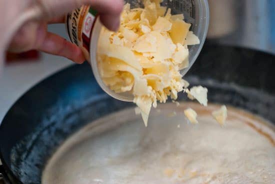 Pouring grated Parmesan cheese into Alfredo sauce recipe.