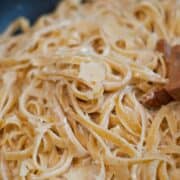 Mixing from scratch fettuccine Alfredo noodles in a large skillet.