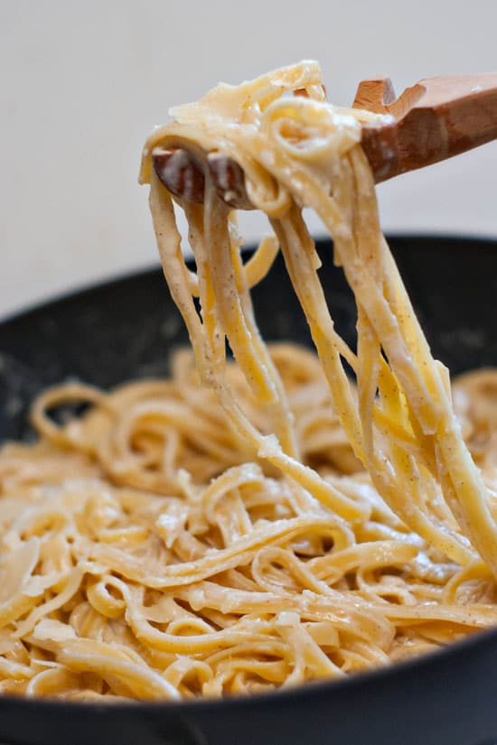 Scooping Homemade Fettuccine Alfredo with a wooden spoon out of a black skillet.