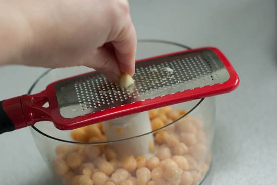 Grating roasted garlic over peeled chickpeas in a food processor. 