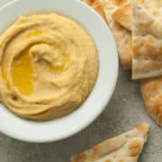 Easy Hummus recipe in a small white bowl with pita bread on the side.